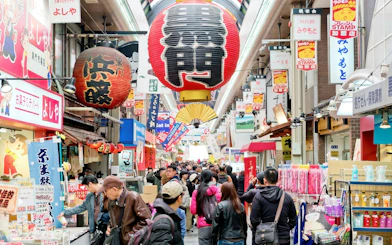 Crowded Kuromon Ichiba Market in Osaka with vibrant signs and lanterns.