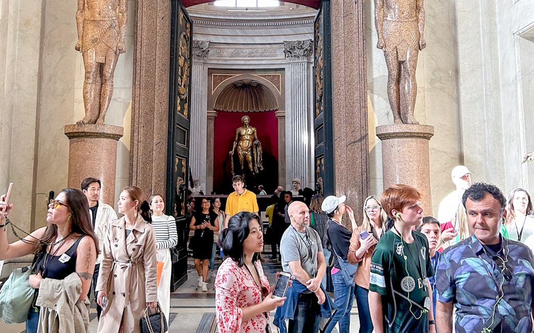 Visitors exploring the Vatican Museums entrance with statues and ornate doorway.