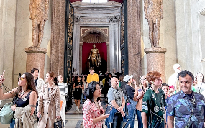 Visitors exploring the Vatican Museums entrance with statues and ornate doorway.