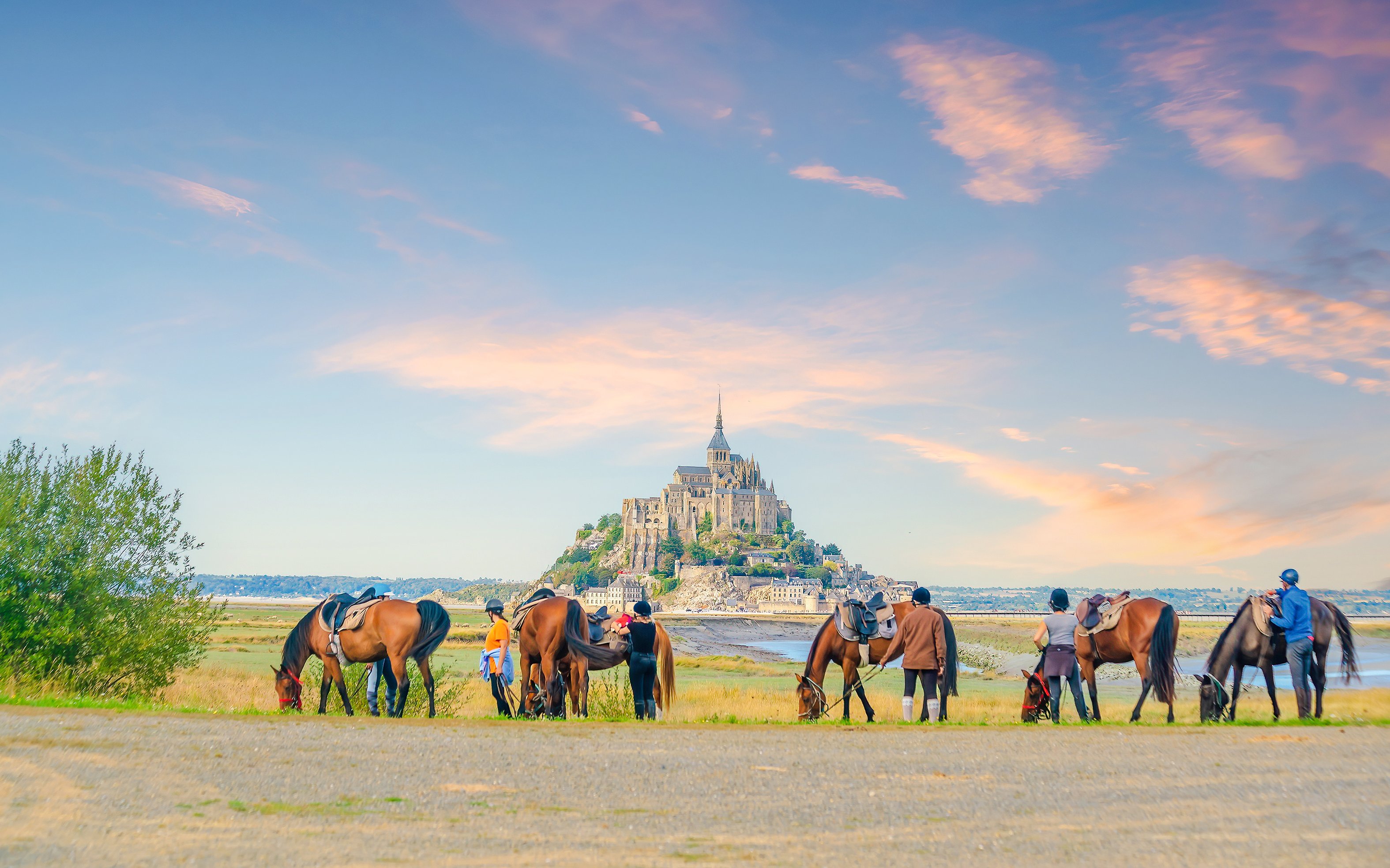 Horseback riders near Mont Saint Michel at sunset.
