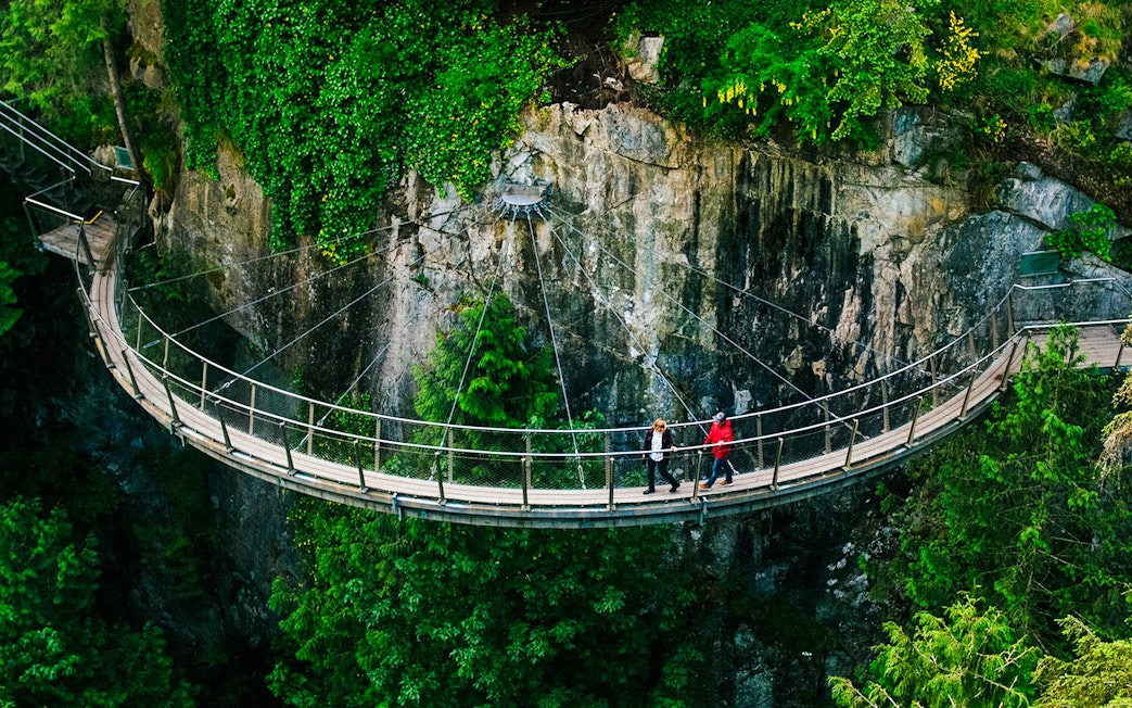 Visitors walking on the Capilano Suspension Bridge in Vancouver, surrounded by lush greenery.