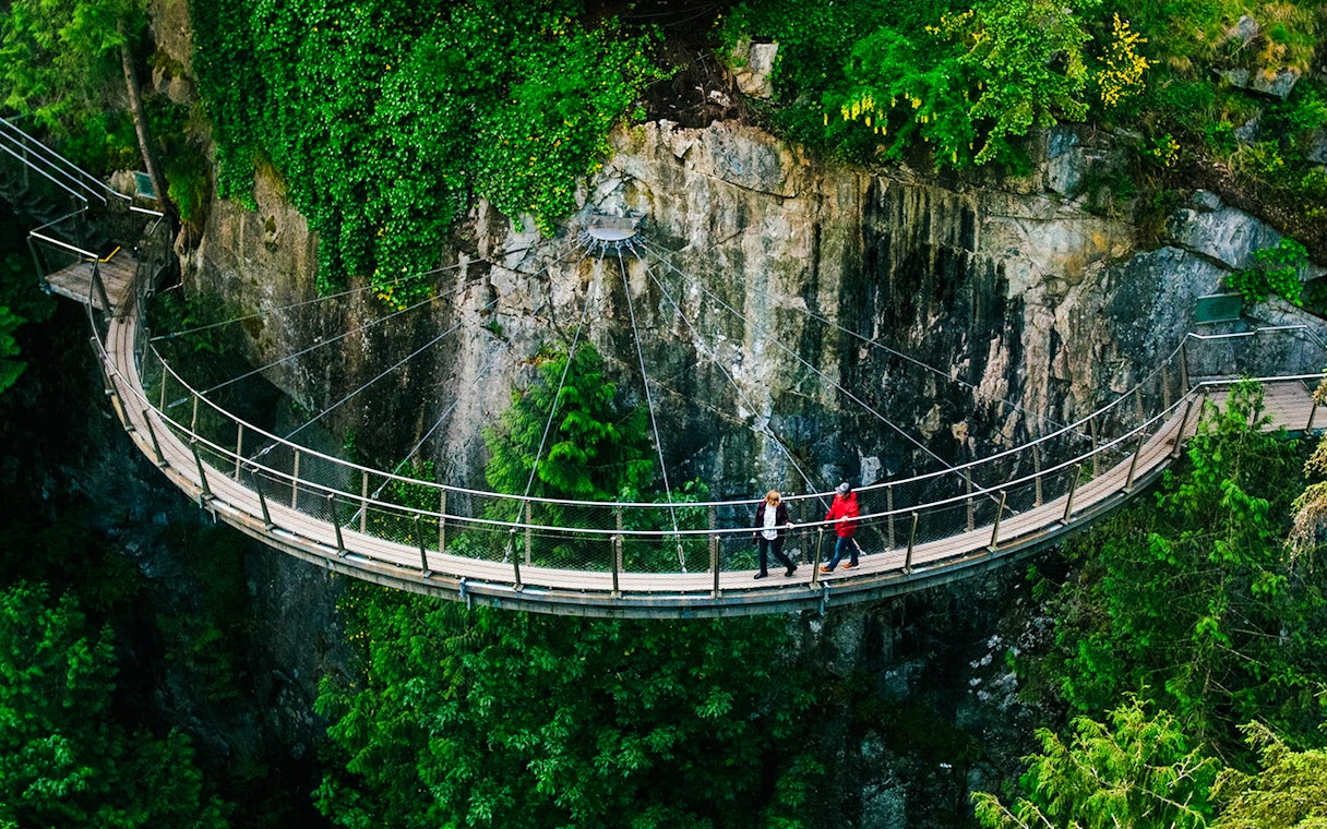 Visitors walking on the Capilano Suspension Bridge in Vancouver, surrounded by lush greenery.