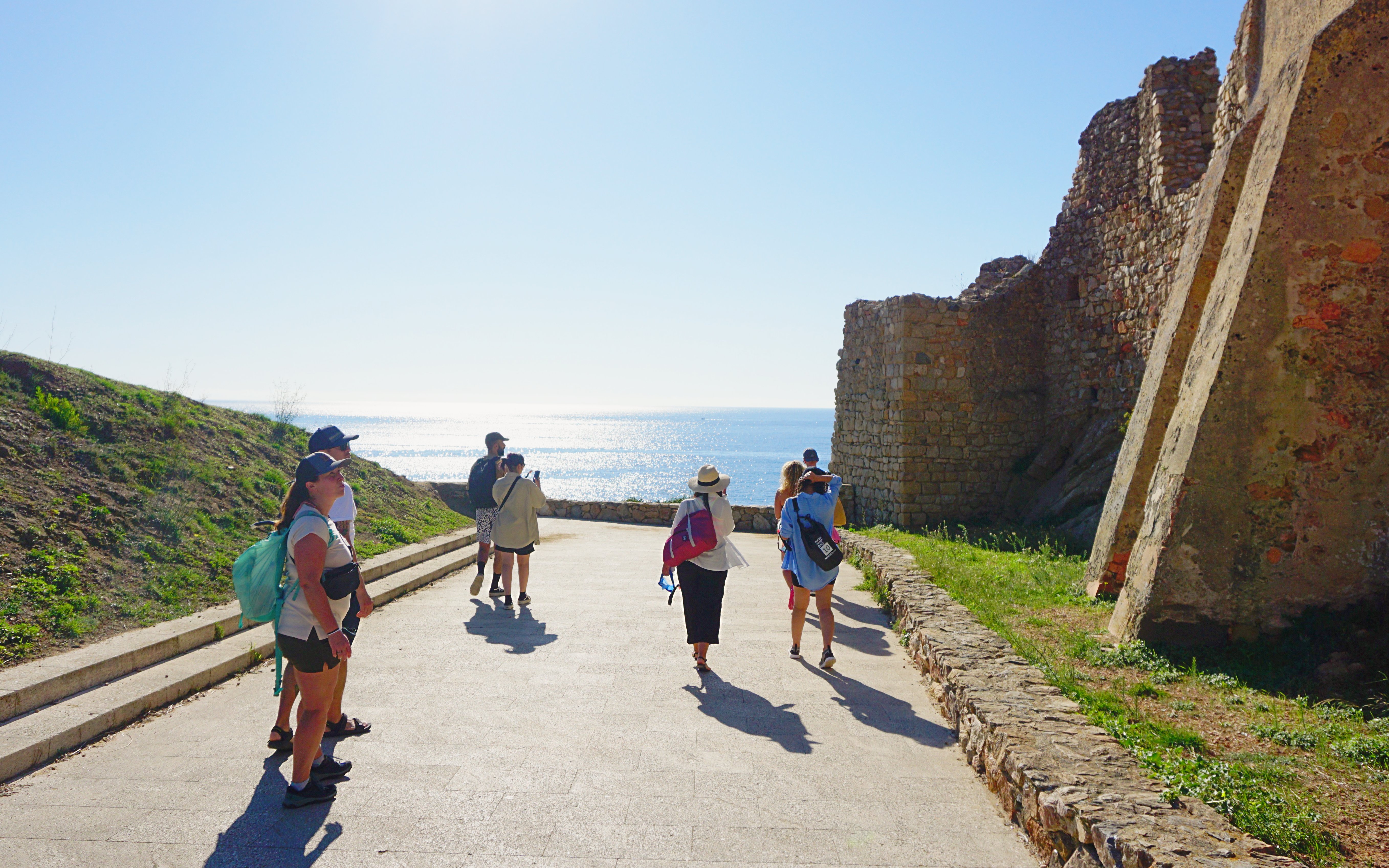 Tourists exploring Castell De Sant Esteve ruins with sea view in the background.