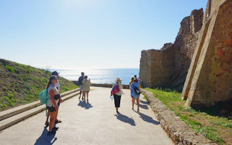 Tourists exploring Castell De Sant Esteve ruins with sea view in the background.