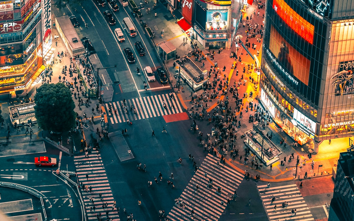 Aerial view of Shibuya Crossing from Shibuya Sky Deck, Tokyo, with bustling crowds and illuminated buildings.