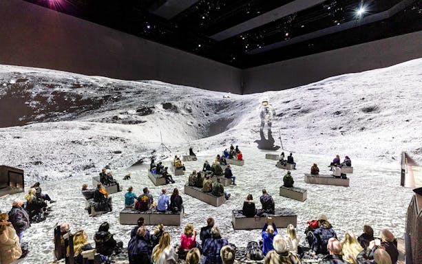 Visitors seated at The Moonwalkers Exhibition, Atelier des Lumières, viewing a lunar landscape projection.
