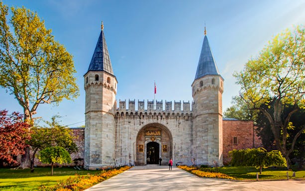 Topkapi Palace entrance with twin towers in Istanbul, Turkey, surrounded by trees.