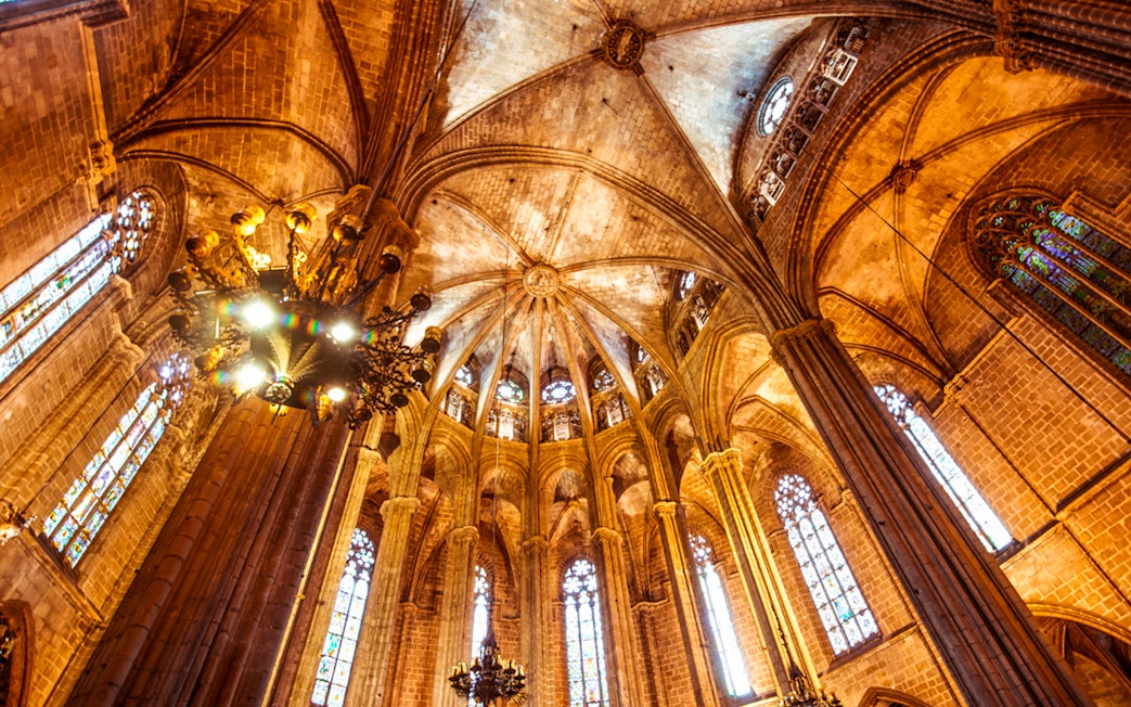 Interior view of the Cathedral of Barcelona's vaulted ceiling and stained glass windows.