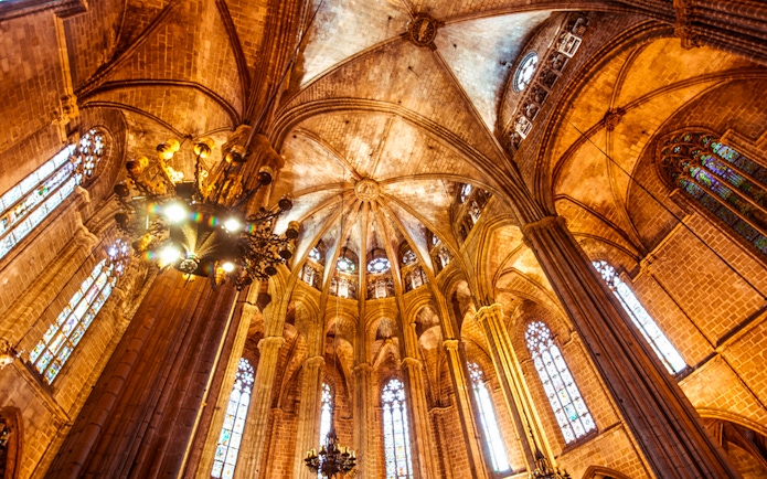 Interior view of the Cathedral of Barcelona's vaulted ceiling and stained glass windows.