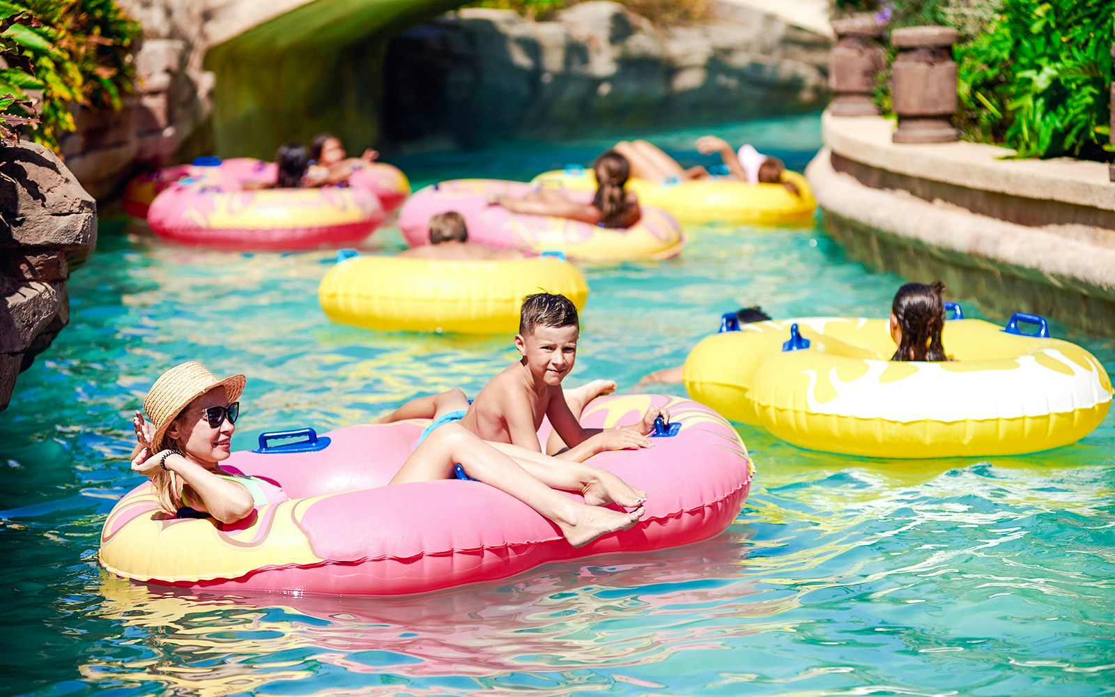 Families enjoying a lazy river ride in colorful inflatable tubes.