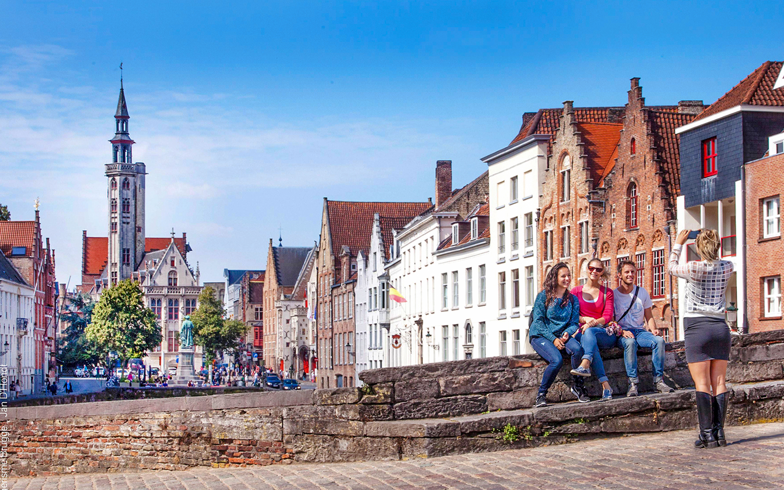 Guests posing for a photo by the canals in Bruges, with historic buildings in the background.