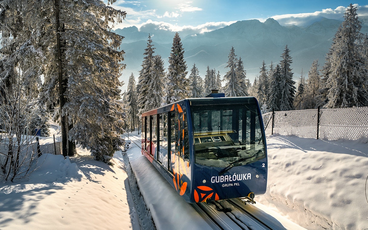 Funicular train ascending snow-covered Gubałówka Hill near Krakow, surrounded by winter forest.