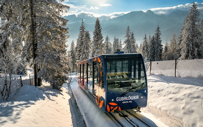 Funicular train ascending snow-covered Gubałówka Hill near Krakow, surrounded by winter forest.