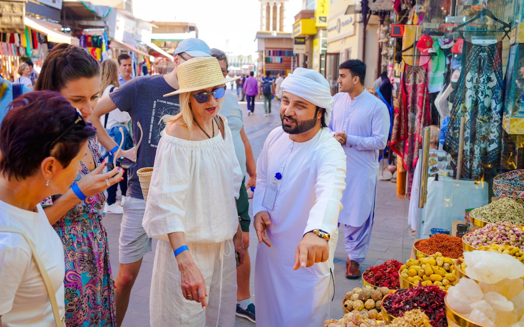 Guide interacting with tourists at a spice stall in a bustling local market.
