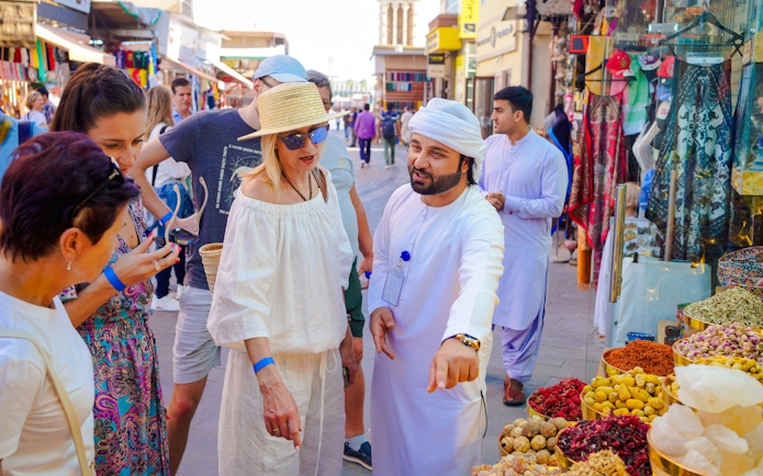 Guide interacting with tourists at a spice stall in a bustling local market.