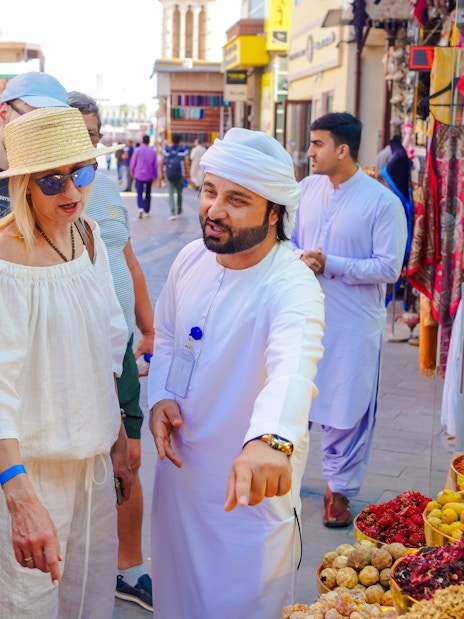 Guide interacting with tourists at a spice stall in a bustling local market.