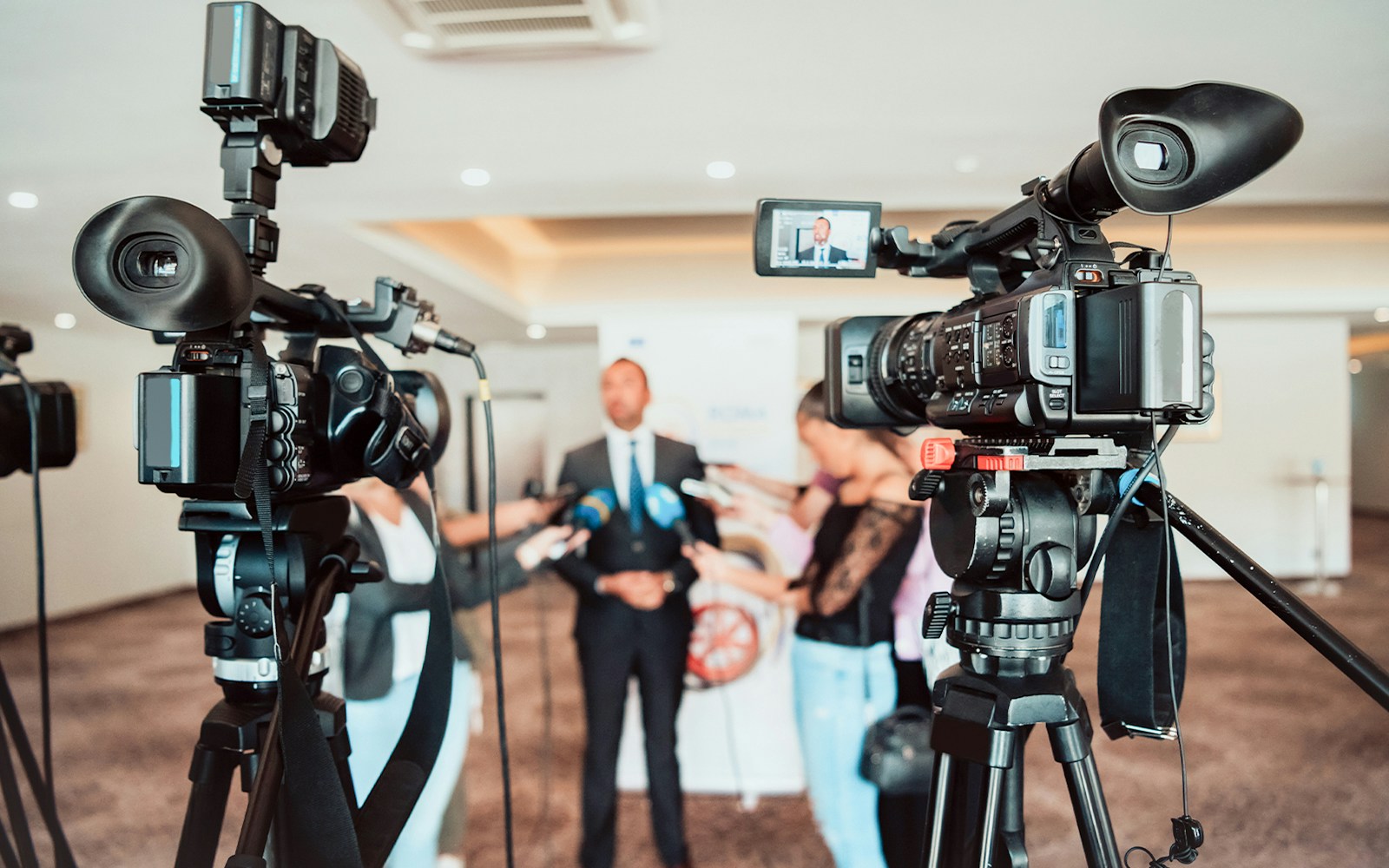 Broadcast television camera setup with lighting capturing a press conference.
