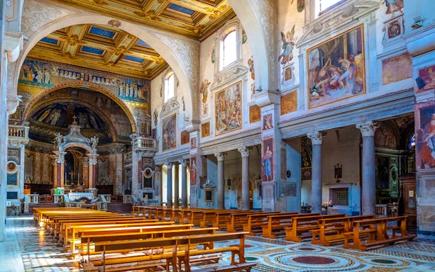 Panoramic view of the Basilica of Saint Praxedes interior with frescoes and wooden pews.