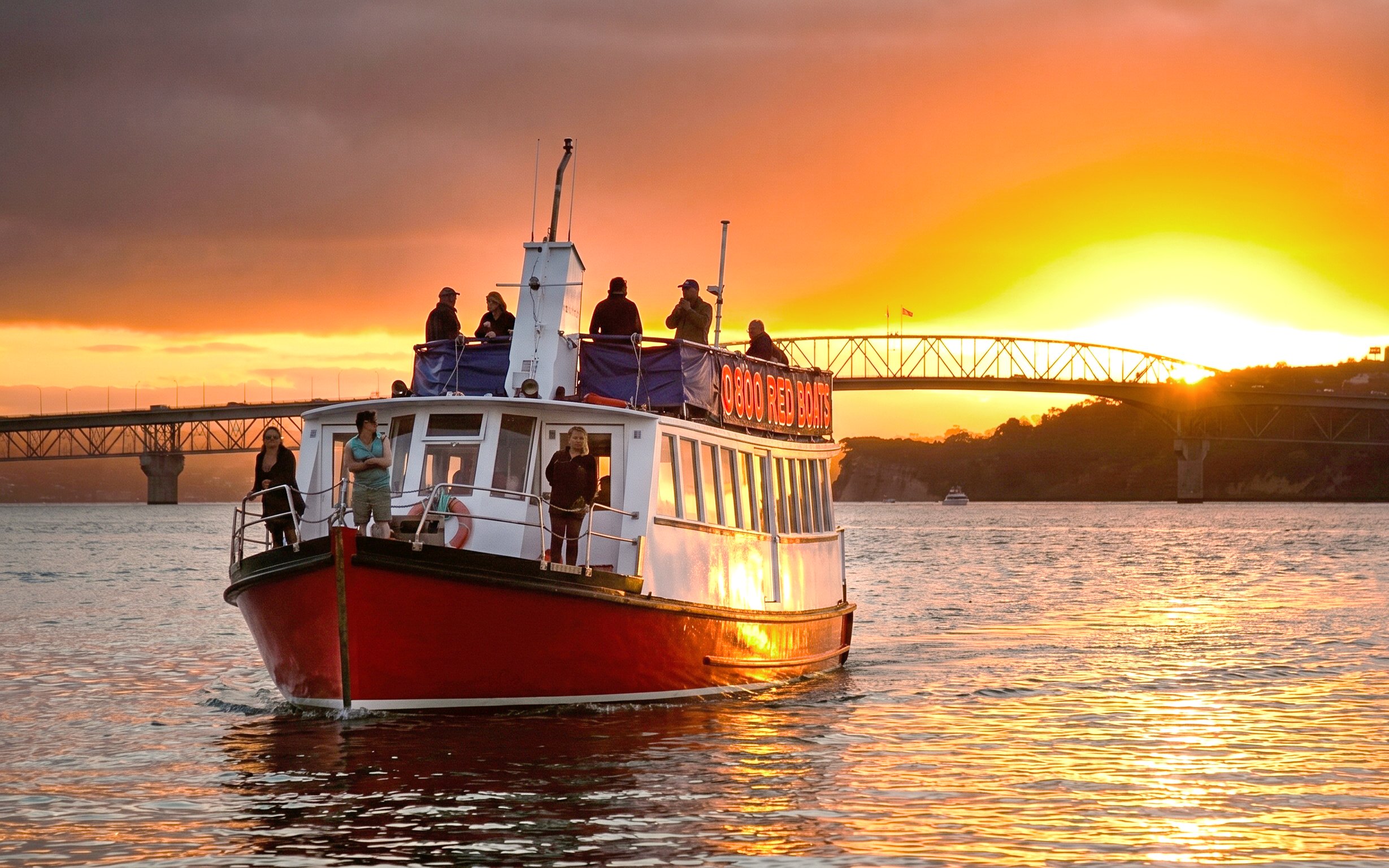 Harbour cruise boat at sunset near Auckland Bridge.