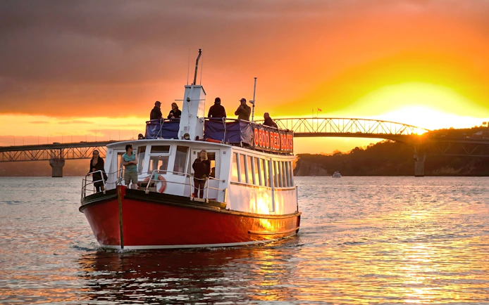 Harbour cruise boat at sunset near Auckland Bridge.