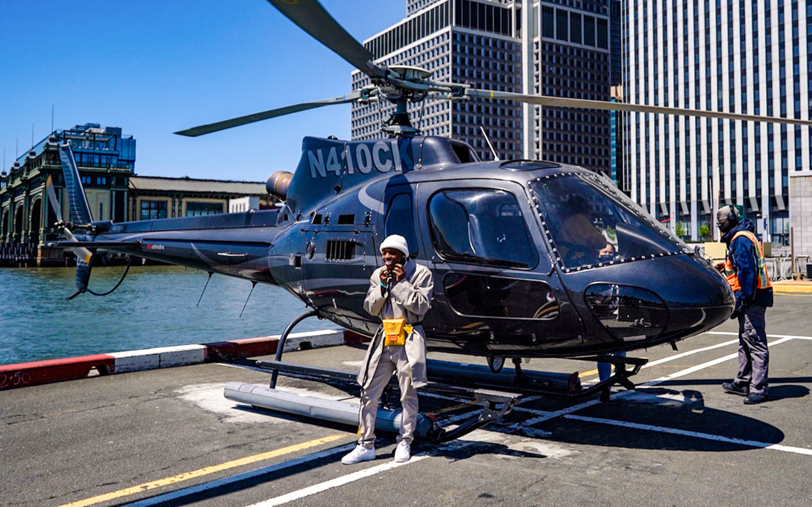 Helicopter parked at New York City pier with people nearby.