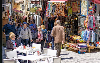 Street market in Albaicin, Granada, with tourists exploring shops and outdoor cafes.