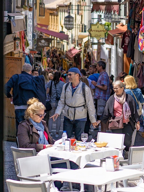 Street market in Albaicin, Granada, with tourists exploring shops and outdoor cafes.
