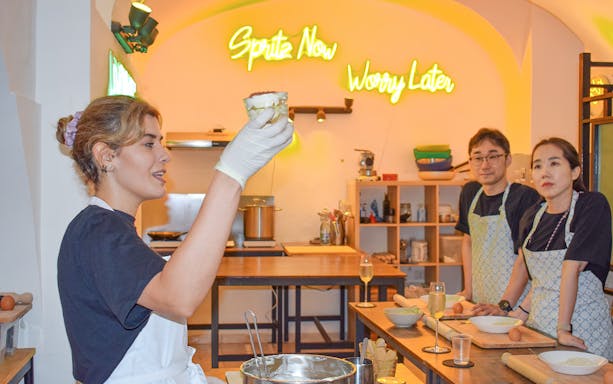 Instructor demonstrating tiramisu preparation in a cooking class with participants observing.