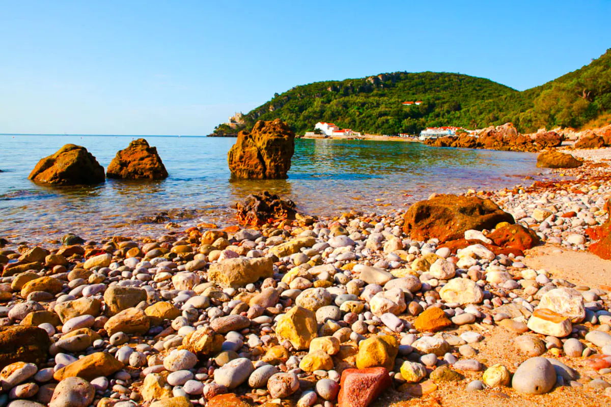 Rocky beach with clear water and distant hills in Arrábida, Portugal.