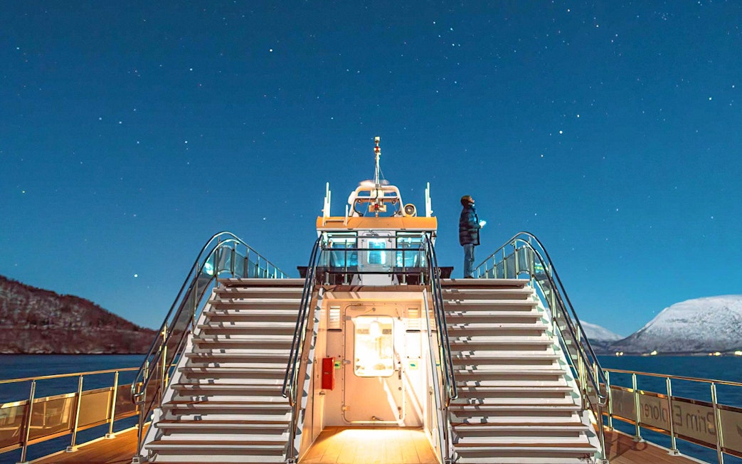 Cruise ship deck under starry sky in Tromso, Norway, with person observing the Northern Lights.