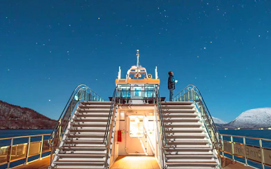 Cruise ship deck under starry sky in Tromso, Norway, with person observing the Northern Lights.