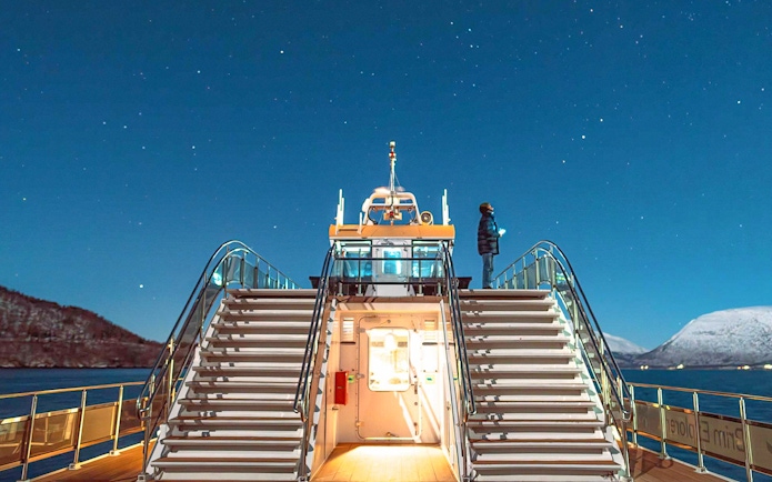 Cruise ship deck under starry sky in Tromso, Norway, with person observing the Northern Lights.