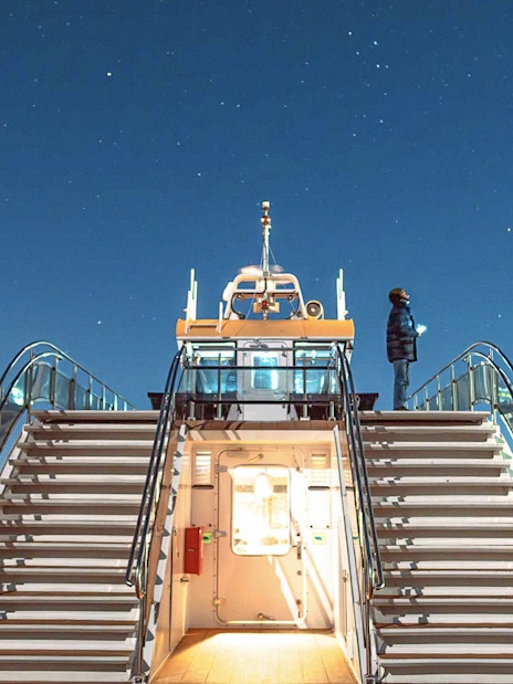 Cruise ship deck under starry sky in Tromso, Norway, with person observing the Northern Lights.