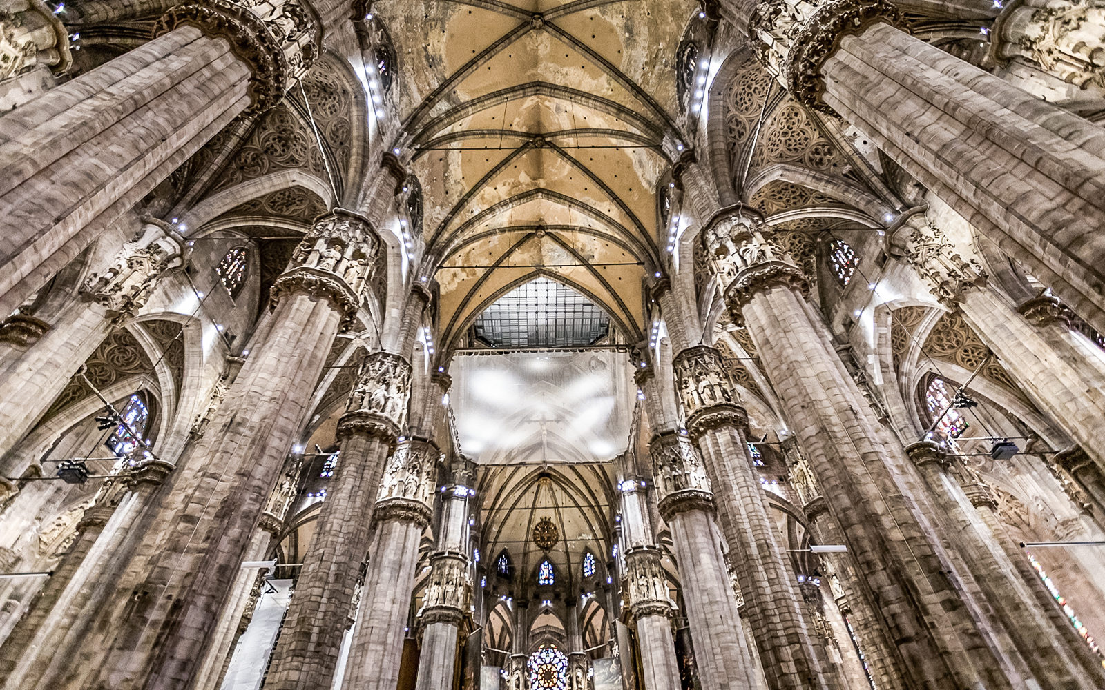 Interiors of Duomo Cathedral in Milan showcasing ornate columns and vaulted ceilings.