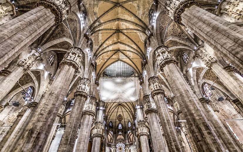 Interiors of Duomo Cathedral in Milan showcasing ornate columns and vaulted ceilings.