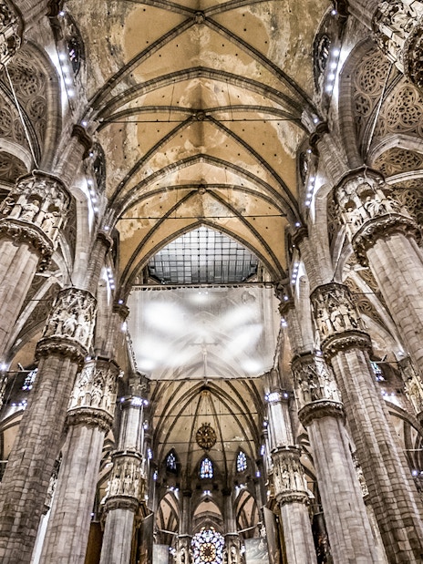 Interiors of Duomo Cathedral in Milan showcasing ornate columns and vaulted ceilings.
