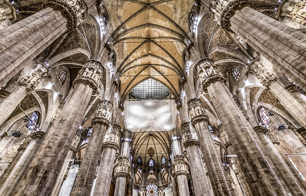 Interiors of Duomo Cathedral in Milan showcasing ornate columns and vaulted ceilings.