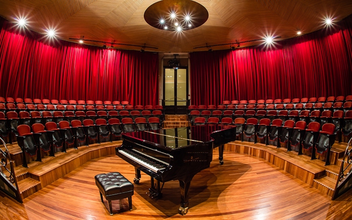 Grand piano on stage at Palau de la Música Catalana, Barcelona, with red seats and curtains.