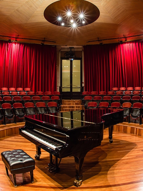 Grand piano on stage at Palau de la Música Catalana, Barcelona, with red seats and curtains.