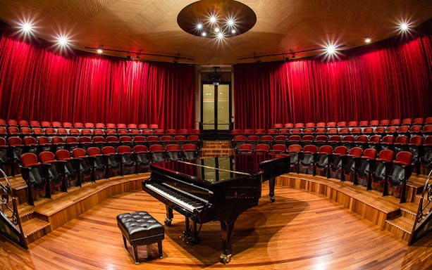 Grand piano on stage at Palau de la Música Catalana, Barcelona, with red seats and curtains.