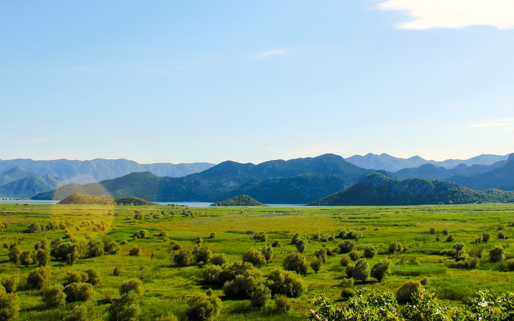 Wide angle view of Lake Skadar with surrounding mountains and lush greenery.