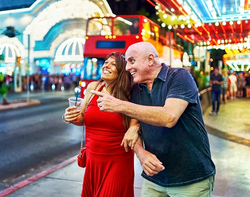 Couple sightseeing on a lively Las Vegas street with neon lights and a red tour bus.