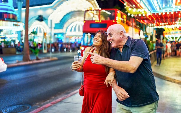 Couple sightseeing on a lively Las Vegas street with neon lights and a red tour bus.