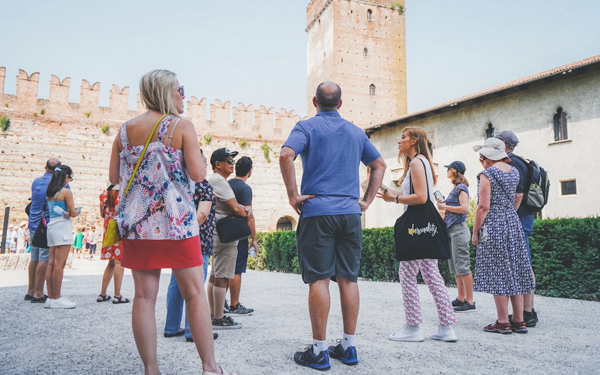 Tour group with guide at Verona Arena, Italy, near ancient stone walls.