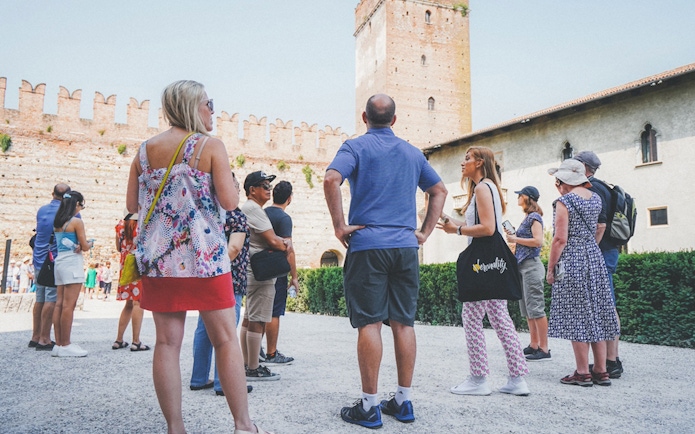 Tour group with guide at Verona Arena, Italy, near ancient stone walls.