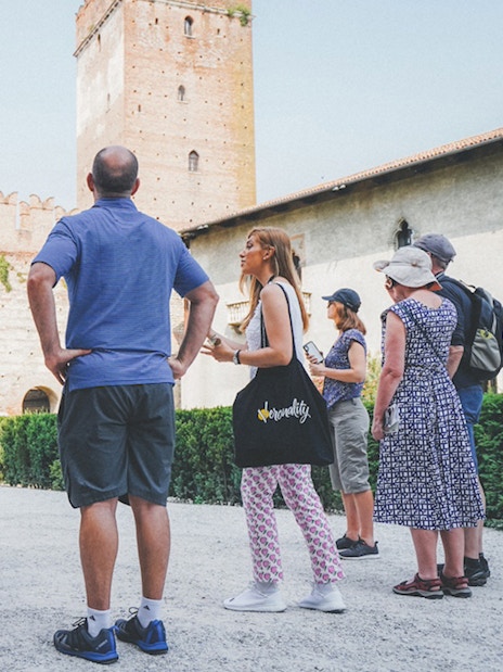 Tour group with guide at Verona Arena, Italy, near ancient stone walls.