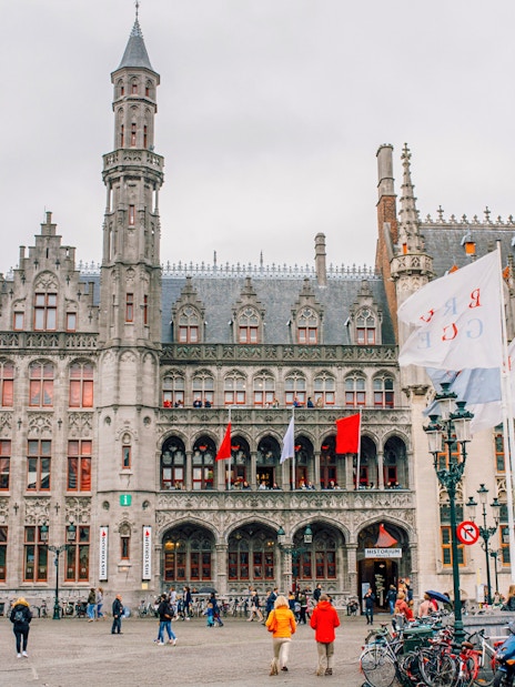 Historium Brugge facade with flags and people in the square.