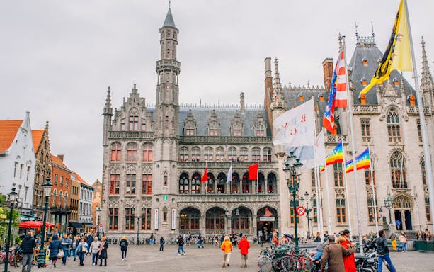 Historium Brugge facade with flags and people in the square.