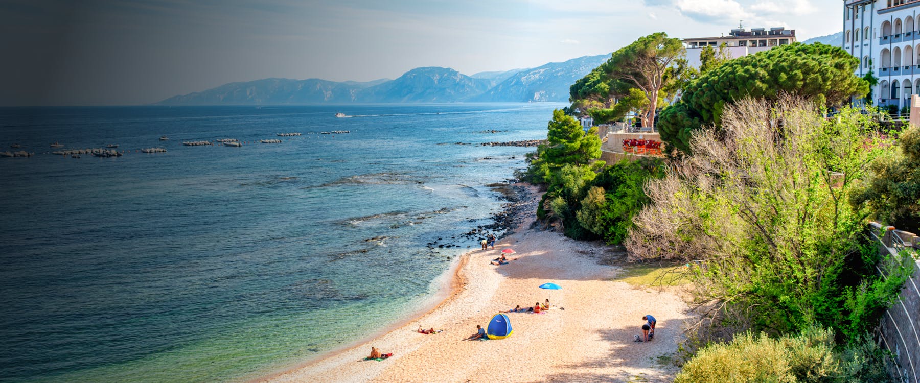 Beach with people relaxing near cliffs and trees, Nuoro, Italy.