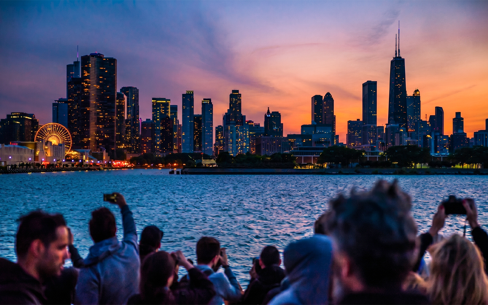 Chicago skyline at sunset viewed from a river cruise, with people taking photos.